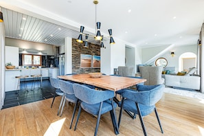 Eine moderne Küche mit Steinrückwand, ein Essbereich mit blauen Stühlen und ein Wohnzimmer mit grauem Sofa.