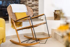 A rocking chair with a woven backrest and a white throw blanket, positioned in a corner of a room with a stone wall and a tiled floor. - Casa Saudade Townhouse - 400m From The Beach (Lagoa)
