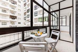 A balcony with a table set for breakfast, white chairs, and a view of adjacent buildings. - Cozy Place Lagos Apartment Beach Couples Nom (Lagos)