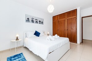A bedroom with a bed, bedside table, lamp, artwork, and wardrobe. - Cozy Place Lagos Apartment Beach Couples Nom (Lagos)