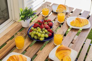 Una mesa de madera con un frutero, croissants y vasos de jugo de naranja.