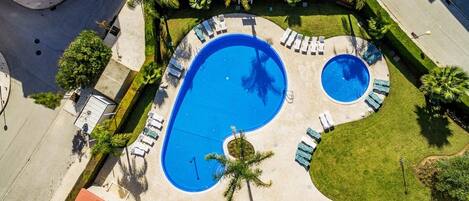 An aerial view of a pool area with two pools, surrounded by lounge chairs and palm trees.