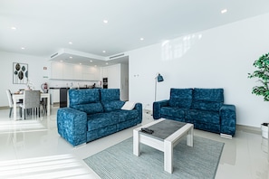 Ein modernes Wohnzimmer mit zwei blauen Sofas, einem Couchtisch und einem Essbereich mit Tisch und Stühlen.
