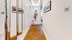 A hallway with a wooden floor, white walls, and framed pictures. - Central 2BR Home Steps to Kensington Palace & Hyde park (London)