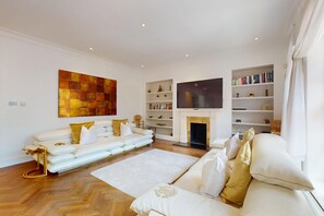 Un salon moderne avec un canapé blanc, une cheminée, un téléviseur à écran plat et des étagères.