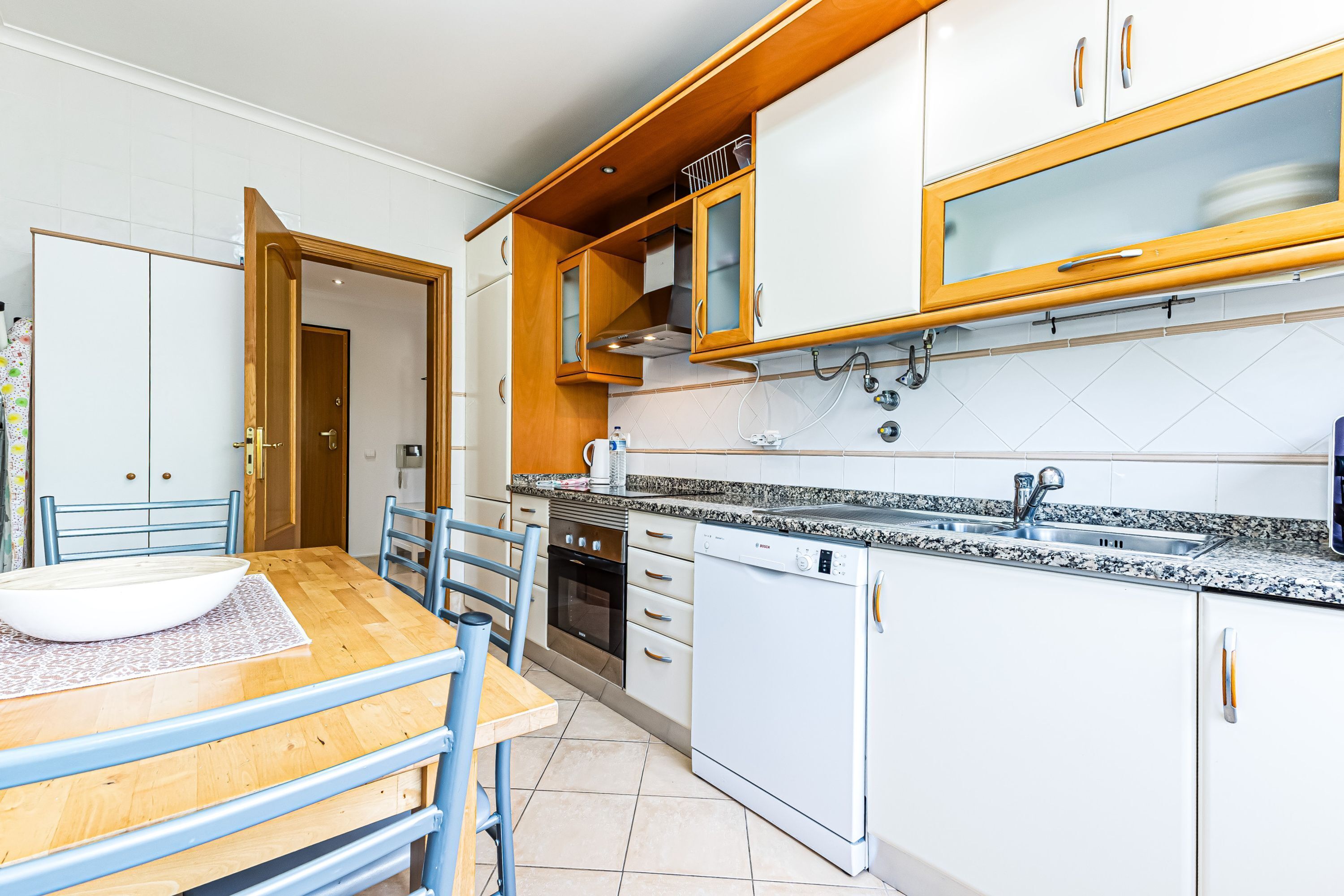 A modern kitchen with white cabinets, a granite countertop, a dishwasher, and a dining area with a wooden table and chairs.