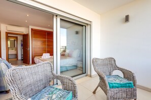 En balkon med fletstole, en skydedør der fører til et soveværelse, og en lille enhed fastgjort på væggen.