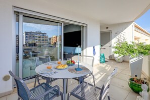 En balkon med et bord dækket til morgenmad, blandt andet croissanter og frugt, samt en potteplante.