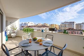 En balkon med et bord dækket til morgenmad, inklusiv tallerkener, glas og en skål med frugt.