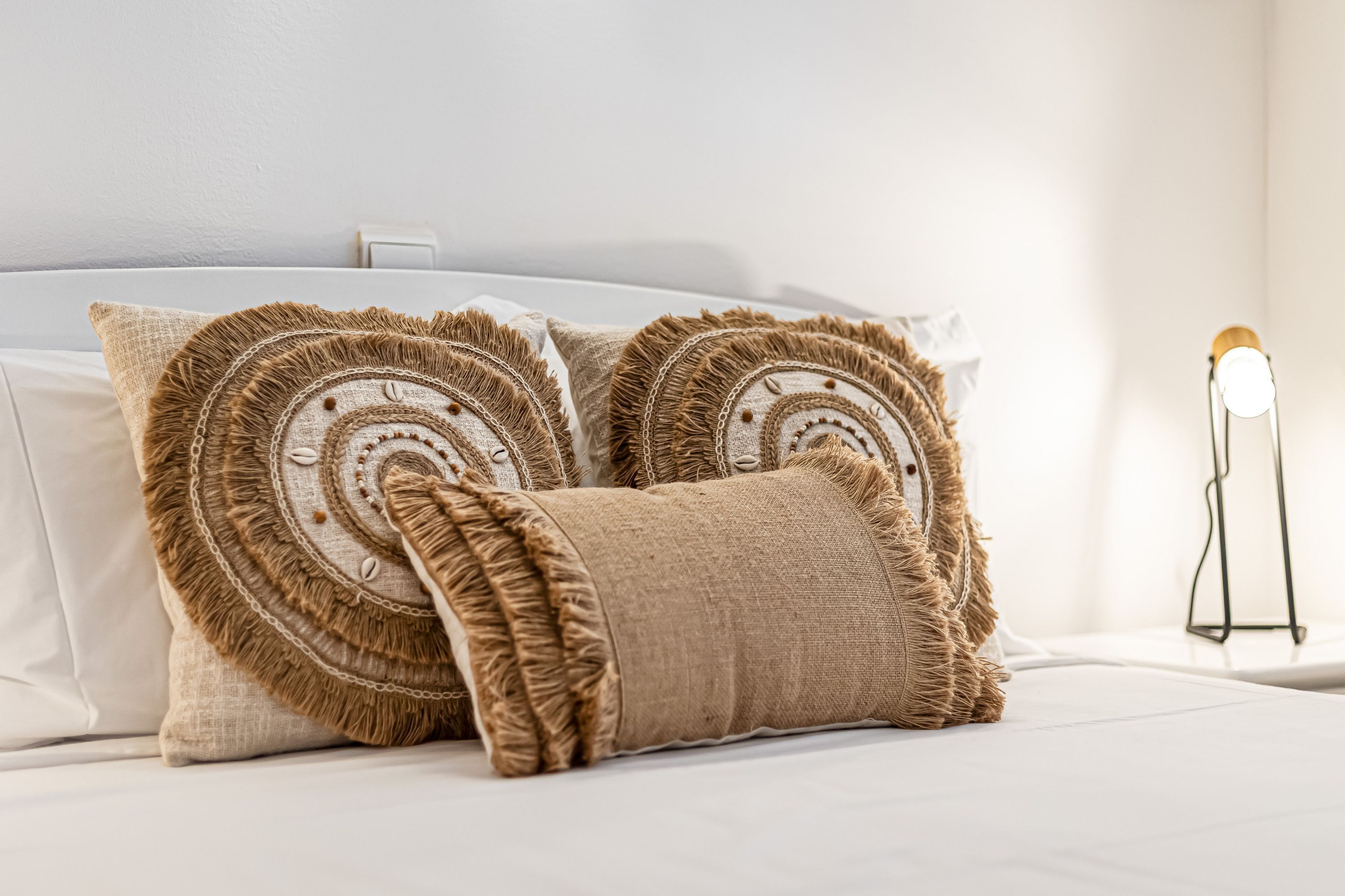 Una cama con ropa blanca y almohadones decorativos con flecos.
