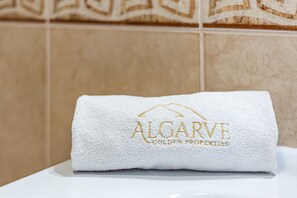 A white towel with 'ALGARVE GOLDEN PROPERTIES' embroidered on it, placed on a white surface against a tiled wall. - Villa Happy Alvor in Portim o (Portimão)