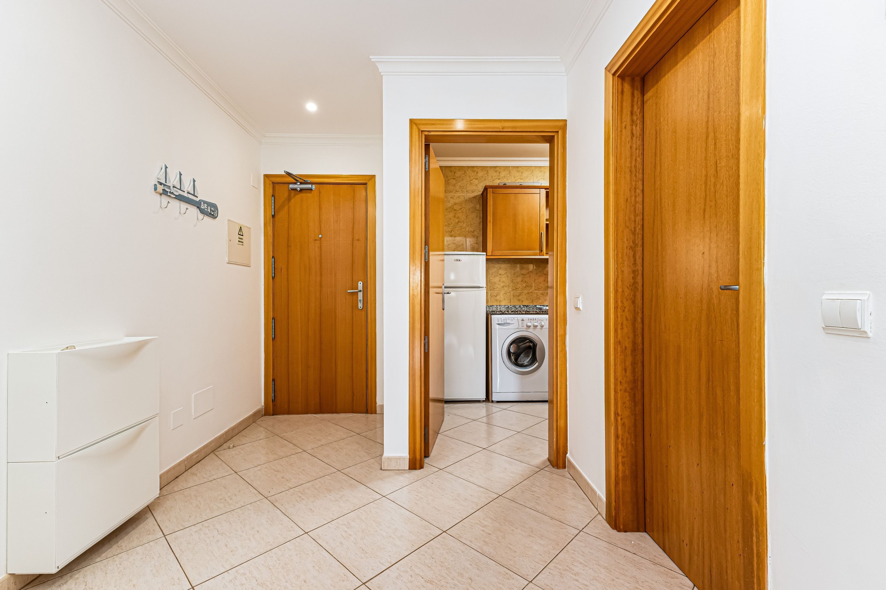 A hallway with a washing machine, a refrigerator, and wooden doors.
