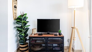 A television on a wooden stand, a potted plant, a lamp, and a wall-mounted sign. - Encosta do Vau in Portim o (Portimão)