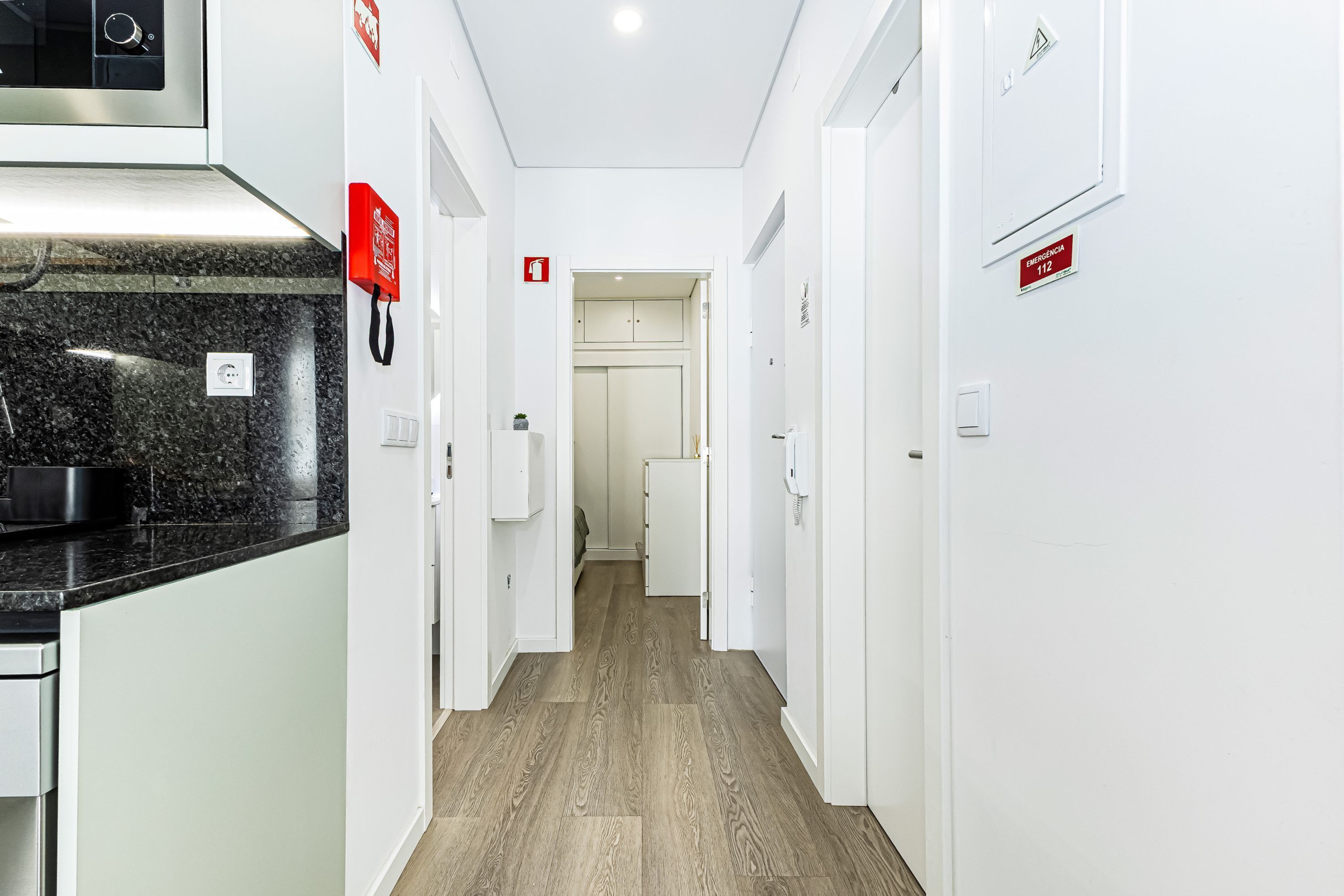 Un pasillo de hotel con área de cocina, paredes blancas y suelo de madera.