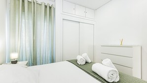 Una habitación de hotel con cama, mesita de noche, lámpara, armario y ventana con cortinas.