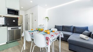 Un espacio habitable compacto con kitchenette, comedor y un sofá gris.