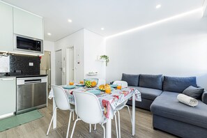 Ein kompakter Wohnbereich mit Küchenzeile, Essplatz und einem grauen Sofa.