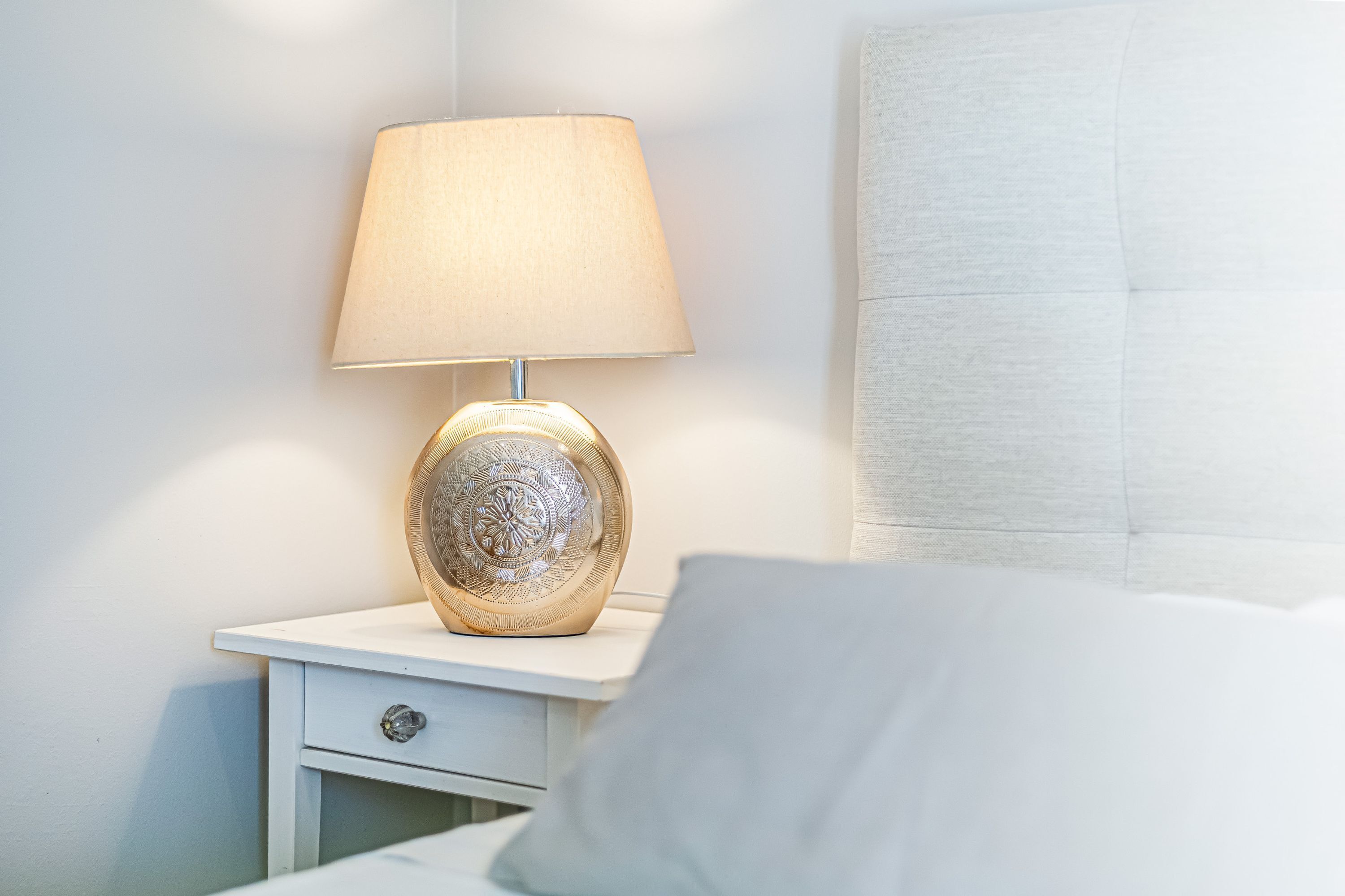Een nachtkastje met een lamp, een lade en een bed met hoofdeinde.