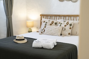 A neatly made bed with patterned pillows, a bedside lamp, a hat, and towels on a dark-colored bedspread. - Casa Oliva Ref gio Rural Contempor neo (Beja)