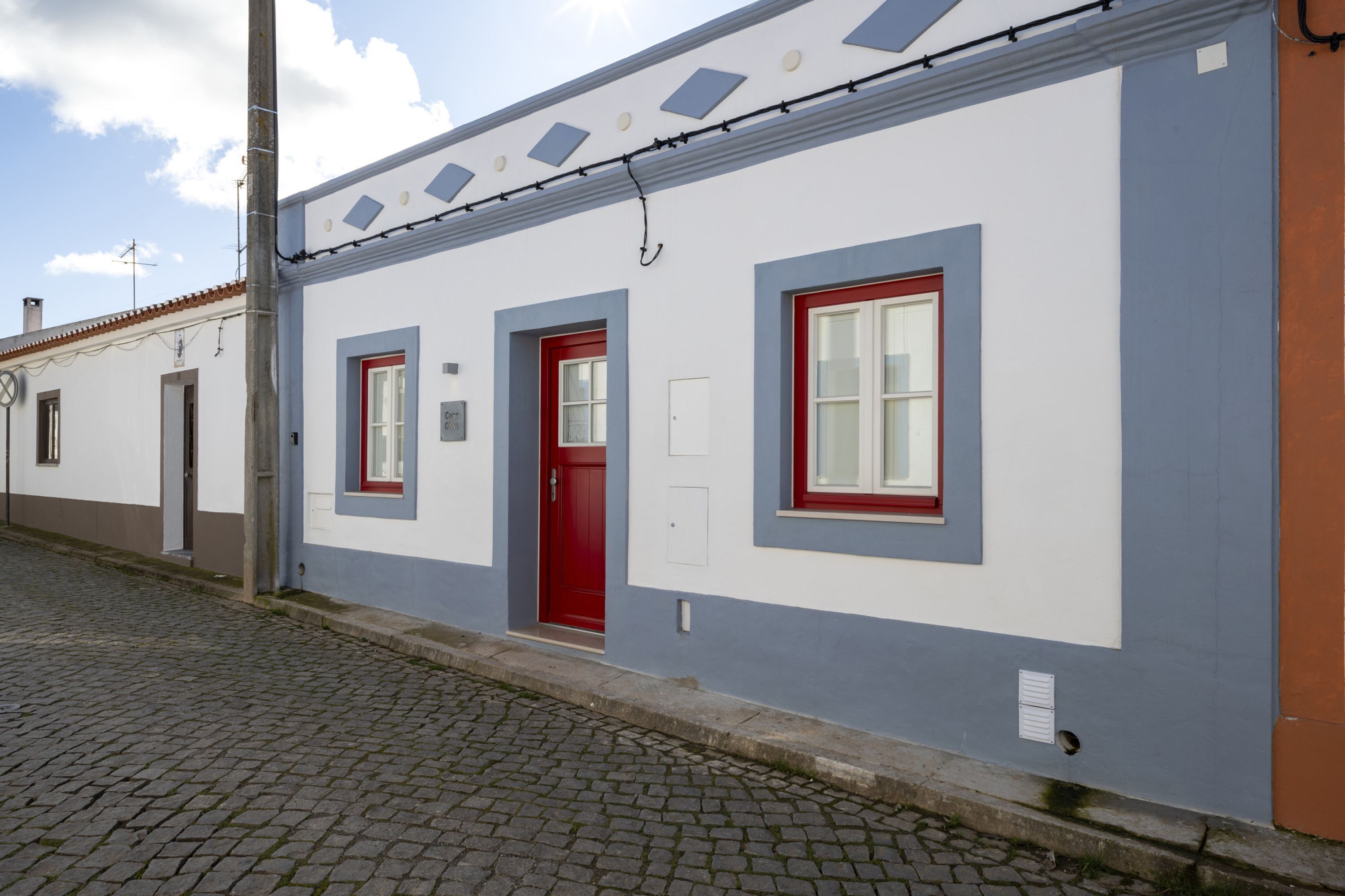 A building with a red door, two windows with red frames, and a cobblestone street.