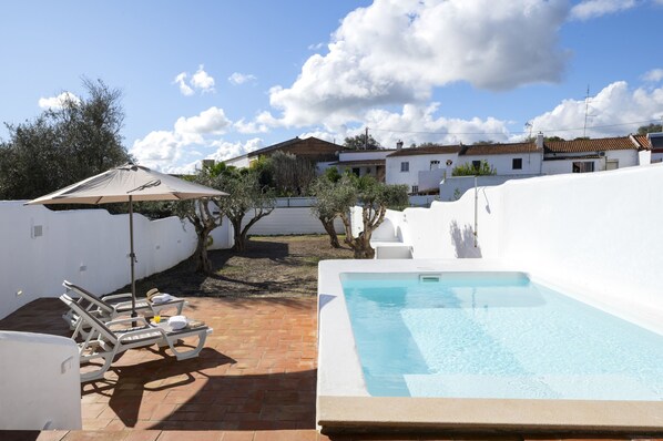 A swimming pool with lounge chairs and an umbrella, surrounded by white walls and a brick patio. - Casa Oliva Ref gio Rural Contempor neo (Beja)