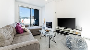 A modern living room with a sofa, ottoman, glass coffee table, and a flat-screen TV. - Casa Colina II Pool BBQ Family Retreat (Silves)