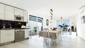 A modern kitchen with a dishwasher, microwave, and dining area with a table and chairs. - Casa Colina II Pool BBQ Family Retreat (Silves)