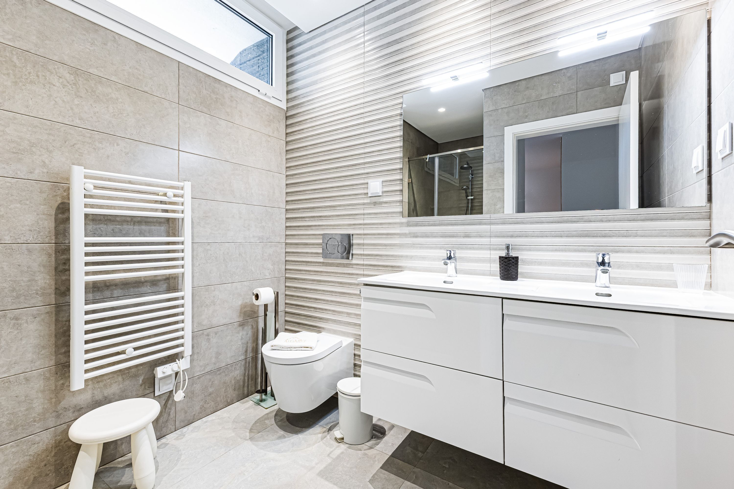 Un baño moderno con un espejo grande, tocador blanco y un perchero para toallas.