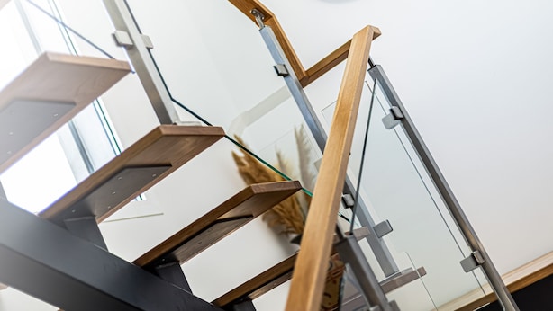 A modern staircase with glass railings and wooden steps, leading to a room with a white wall and a decorative circular wall hanging. - Casa Colina II Pool BBQ Family Retreat (Silves)