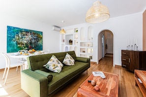 A modern living room with a green sofa, wooden coffee table, and a dining area with white chairs. - Casa Sol Vilamoura (Loulé)