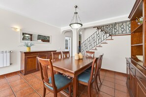 A dining area with a wooden table and chairs, a staircase with a wrought iron railing, and a ceiling light fixture. - Casa Thalassa Portim o (Portimão)