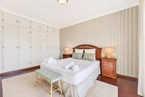 Un dormitorio ordenado con cama, mesitas de noche, un banco y un armario.