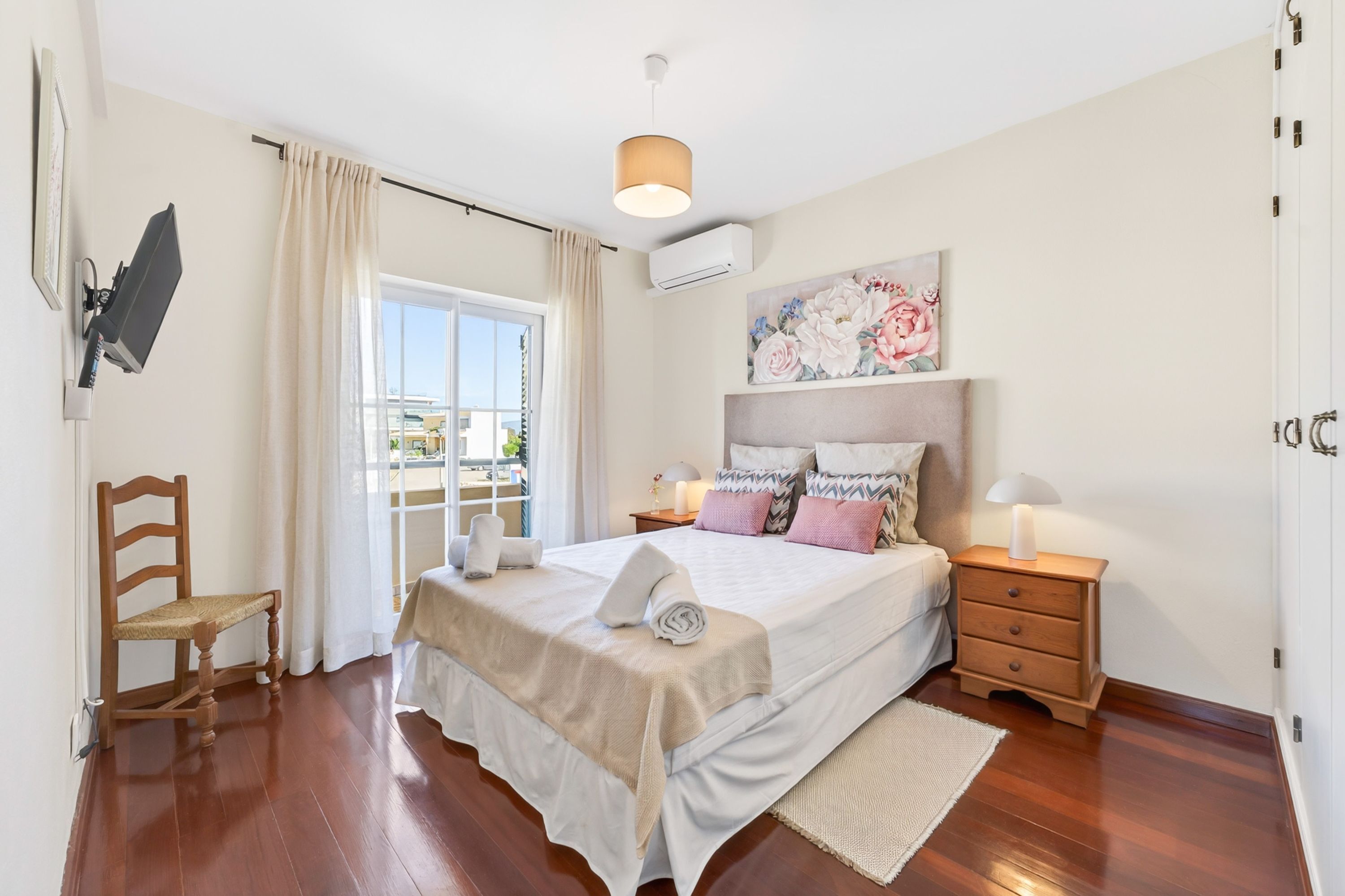 A bedroom with a bed, bedside tables, a chair, a window with curtains, and a ceiling light.