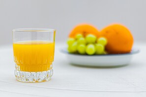 Ein Glas Orangensaft, eine Schale Trauben und eine Orange auf weißer Unterlage.