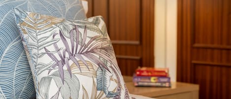Ein Bett mit gemusterten Kissen, einem Holzkopfende und einem Nachttisch mit Büchern.