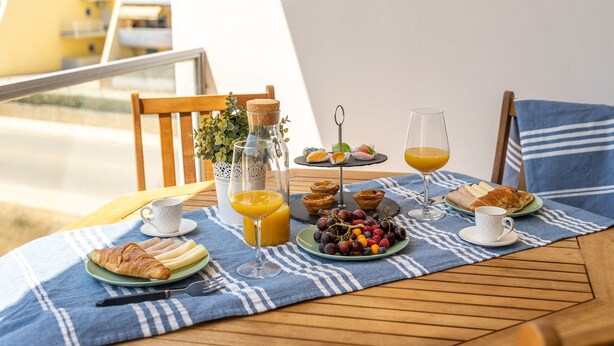 A breakfast setup with croissants, fruit, juice, and a small plant on a balcony table. - Sea La Vie On the Beach City Center Marina (Lagos)