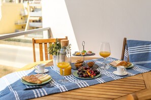 Desayuno con cruasanes, fruta, jugo y una pequeña planta sobre una mesa de balcón.