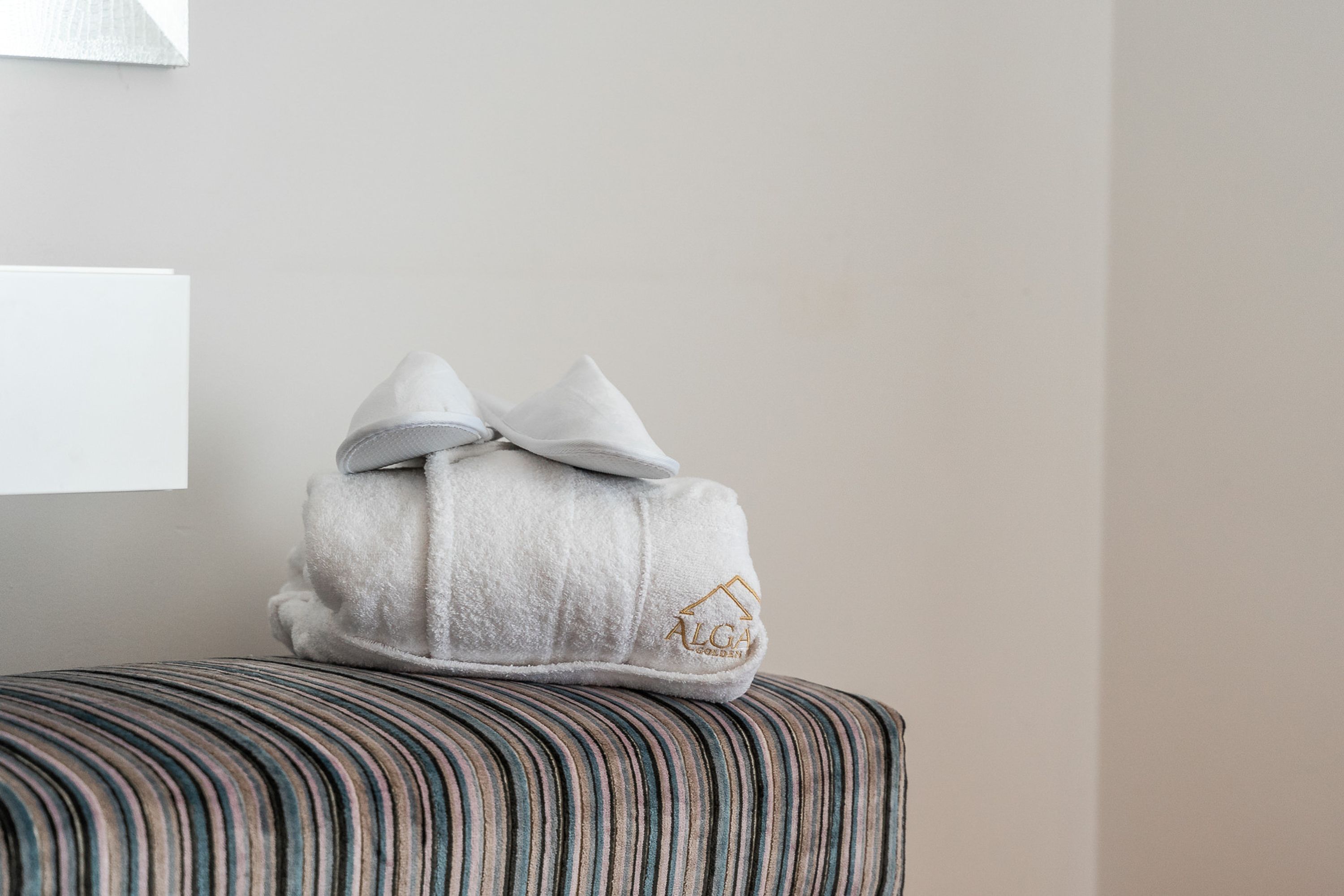 Une serviette blanche ornée du logo d’une maison, posée sur un pouf à rayures.