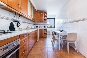 A kitchen with wooden cabinets, a microwave, a kettle, and a dining area with a table and chairs. - Sea La Vie On the Beach City Center Marina (Lagos)