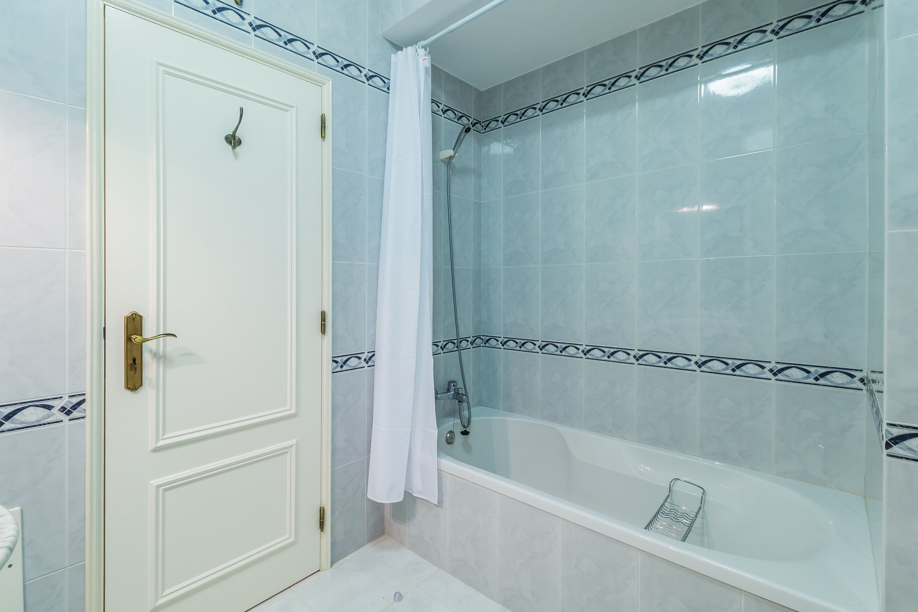 A bathroom with a white door, a shower with a curtain, and a bathtub.