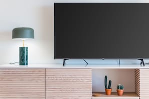 A flat-screen TV mounted on a white wall, a marble lamp on a wooden cabinet, and two potted cacti on a shelf. - Casa da Gal Near Meia Praia Perfect Place w S (Lagos)