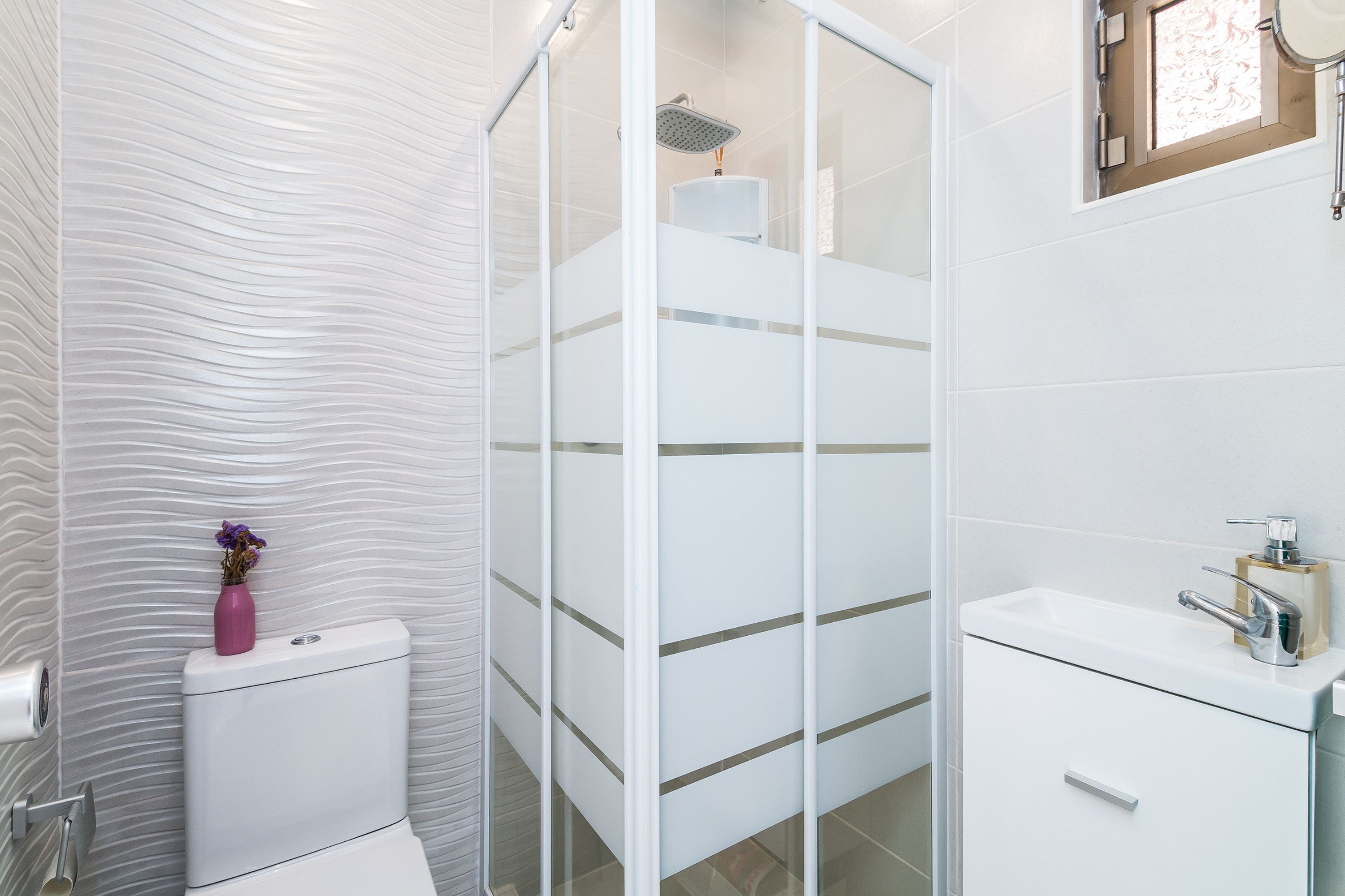 Ein modernes Badezimmer mit Duschabtrennung aus Glas, einer weißen Toilette und einem Waschbecken mit Seifenspender.