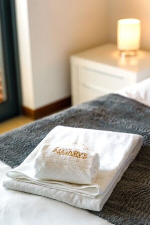 A neatly made bed with a folded white towel and a pillow with 'ALCARVE' embroidered on it. - Marina Village Pool Garage Prime Location AC (Lagos)