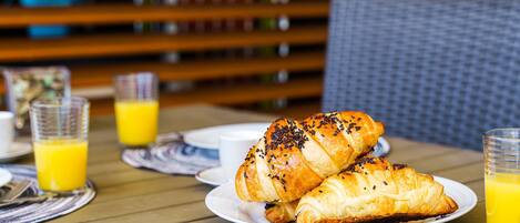 A breakfast setting with croissants on a plate, a glass of orange juice, and a wicker chair in the background.