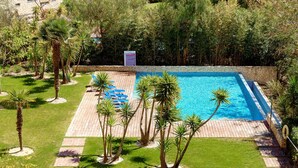 A swimming pool with a stone border, surrounded by palm trees and a paved deck. - Marina Village Pool Garage Prime Location AC (Lagos)