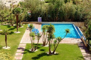 A rectangular swimming pool surrounded by palm trees and a paved deck with lounge chairs. - Marina Village Pool Garage Prime Location AC (Lagos)