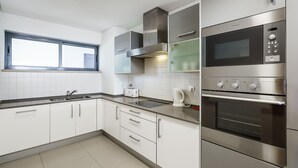 A modern kitchen with stainless steel appliances, a window, and white cabinetry. - Marina Village Pool Garage Prime Location AC (Lagos)