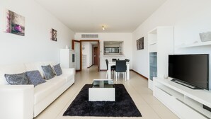 A modern living room with a white sofa, black rug, TV, and dining area. - Marina Village Pool Garage Prime Location AC (Lagos)