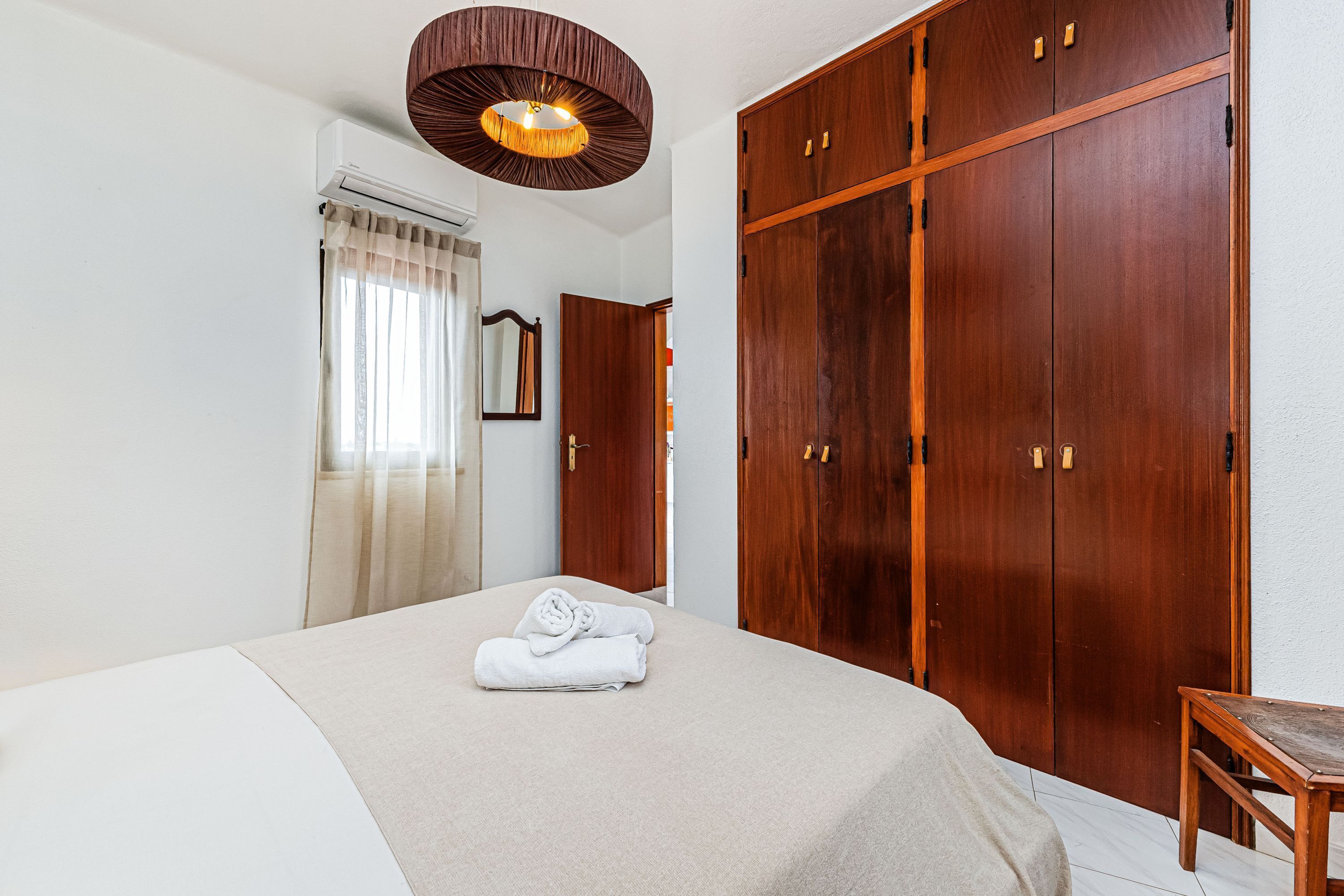Ein Schlafzimmer mit einem Bett, einem Holzschrank, einem Spiegel und einer Pendelleuchte.