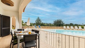 An outdoor dining area with a pool view, including a table with chairs, a drink, and a view of the pool and landscape. - Casa do Vale PET Friendly Pool Lagoa Retreat (Lagoa)